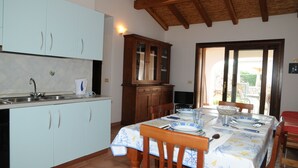 Une cuisine avec des meubles de couleur bleu clair, une table à manger en bois mise avec des assiettes, des verres et des couverts, et un téléviseur posé sur un meuble.