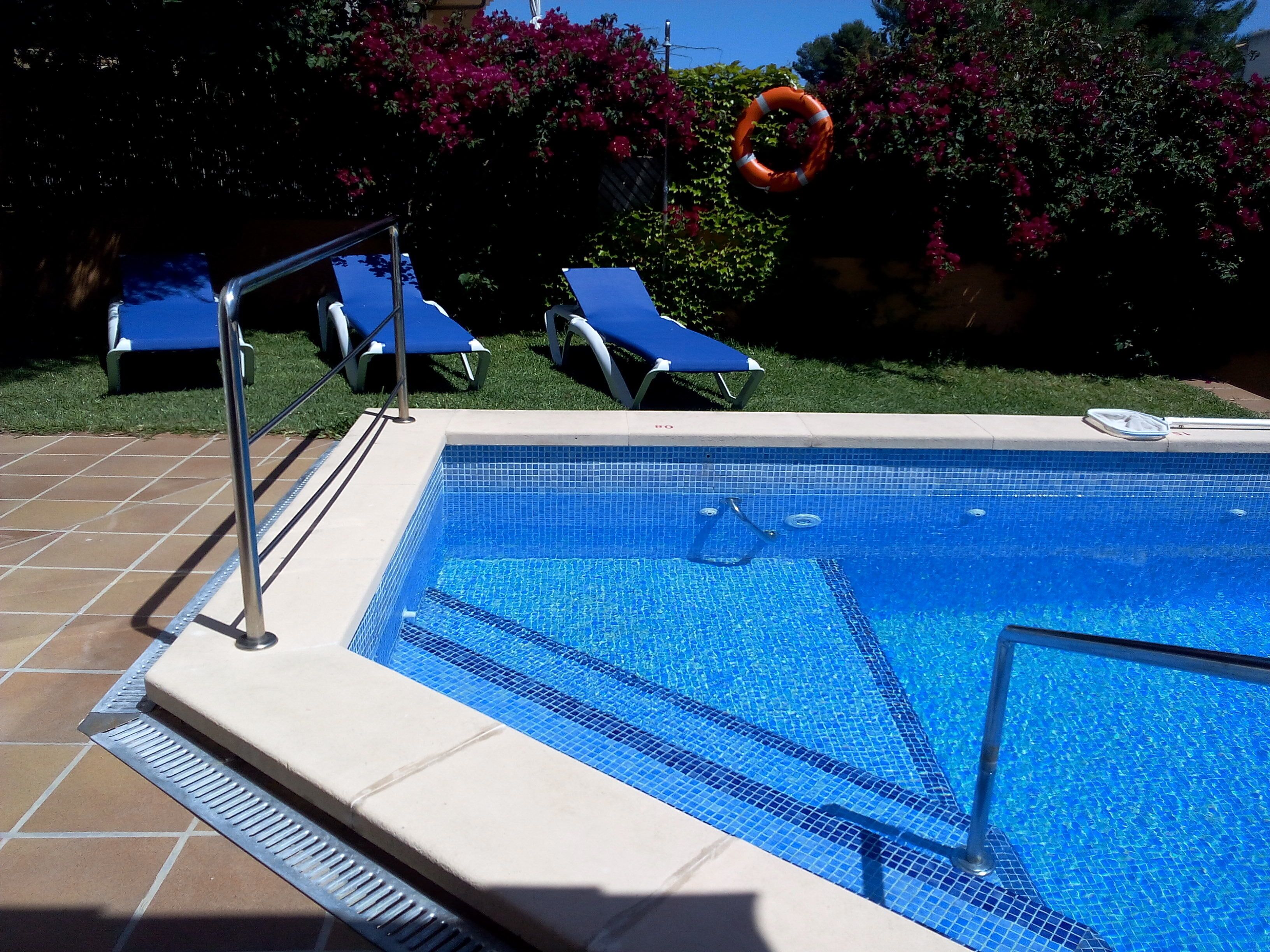Une piscine aux carreaux bleus, avec une échelle et des chaises longues bleues.