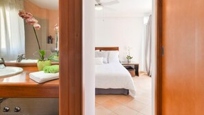 Habitación de hotel con baño, una cama, ventilador de techo y mesita de noche con lámpara.