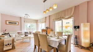 Una sala de estar moderna con comedor, muebles color beige y ventanas amplias.
