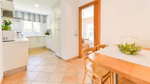 Una cocina moderna con armarios blancos, una mesa de comedor con sillas y una ventana con cortina a rayas.