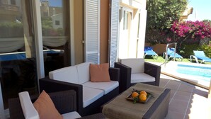 Un patio con mobiliario de mimbre, una mesita con fruta y una piscina al fondo.