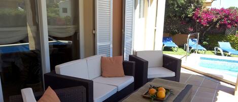 A patio area with wicker furniture, a small table with fruit, and a pool in the background.