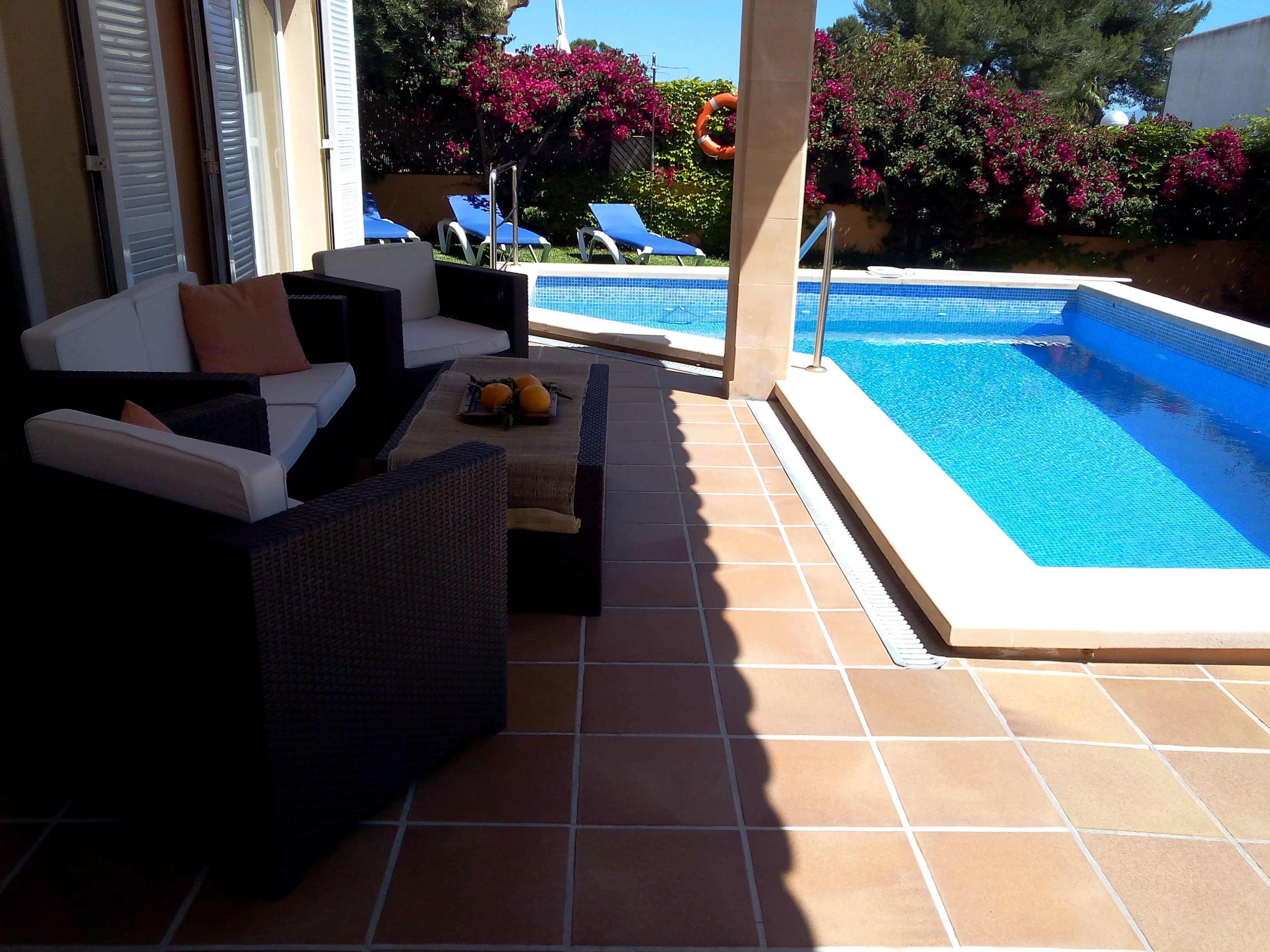 Un espace aménagé au bord de la piscine, avec des meubles d’extérieur, un sol carrelé et une piscine.