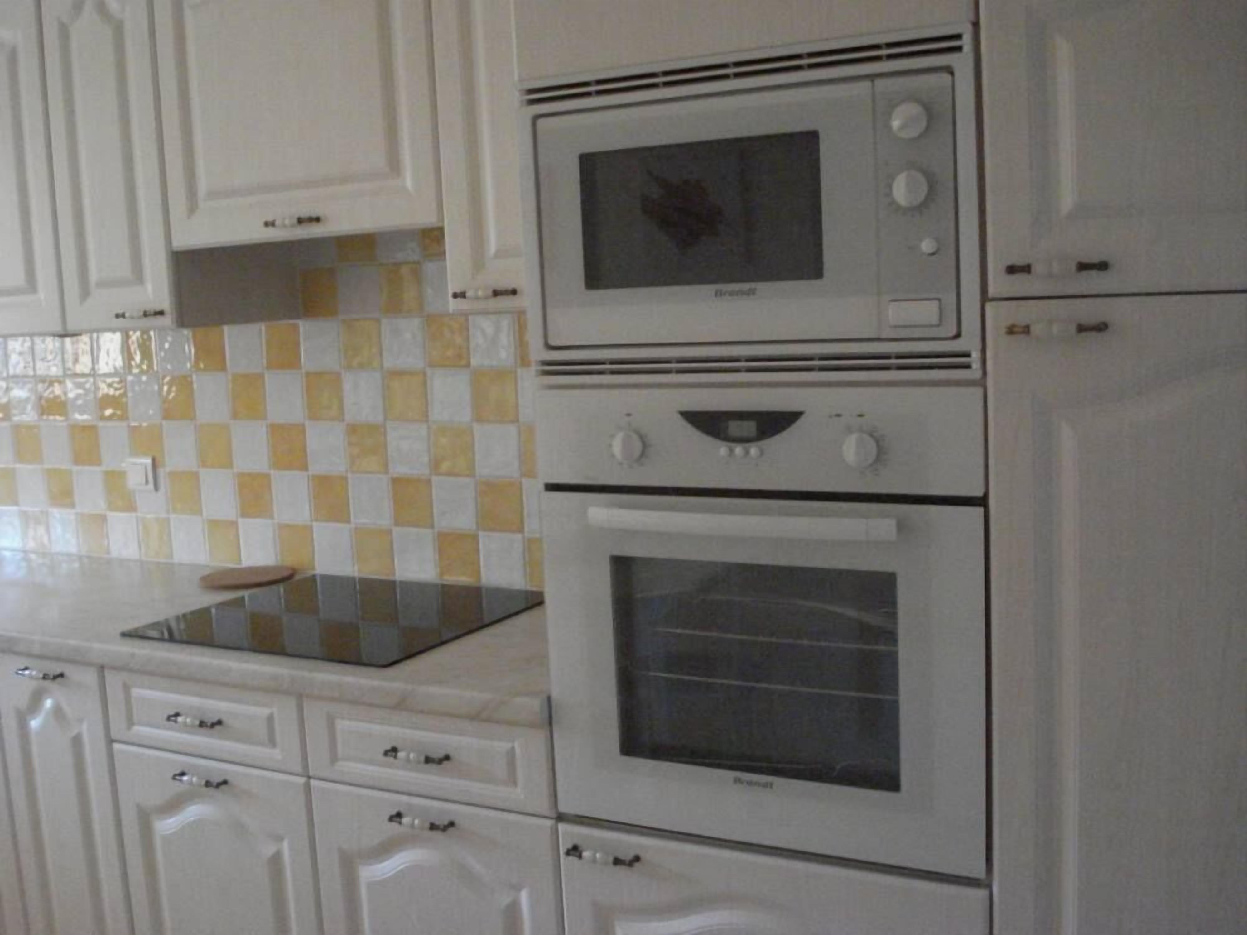 Une cuisine avec des meubles blancs, un four à micro-ondes, un four traditionnel et un pare-feu à carreaux.
