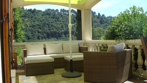 A covered outdoor seating area with wicker furniture and a yellow umbrella, overlooking a forested hillside.