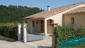 A villa with a tiled roof, a gated entrance, and a view of a forested hill.