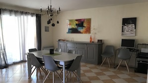 A dining area with a table and chairs, a kitchen area with cabinets and a countertop, and a painting on the wall.