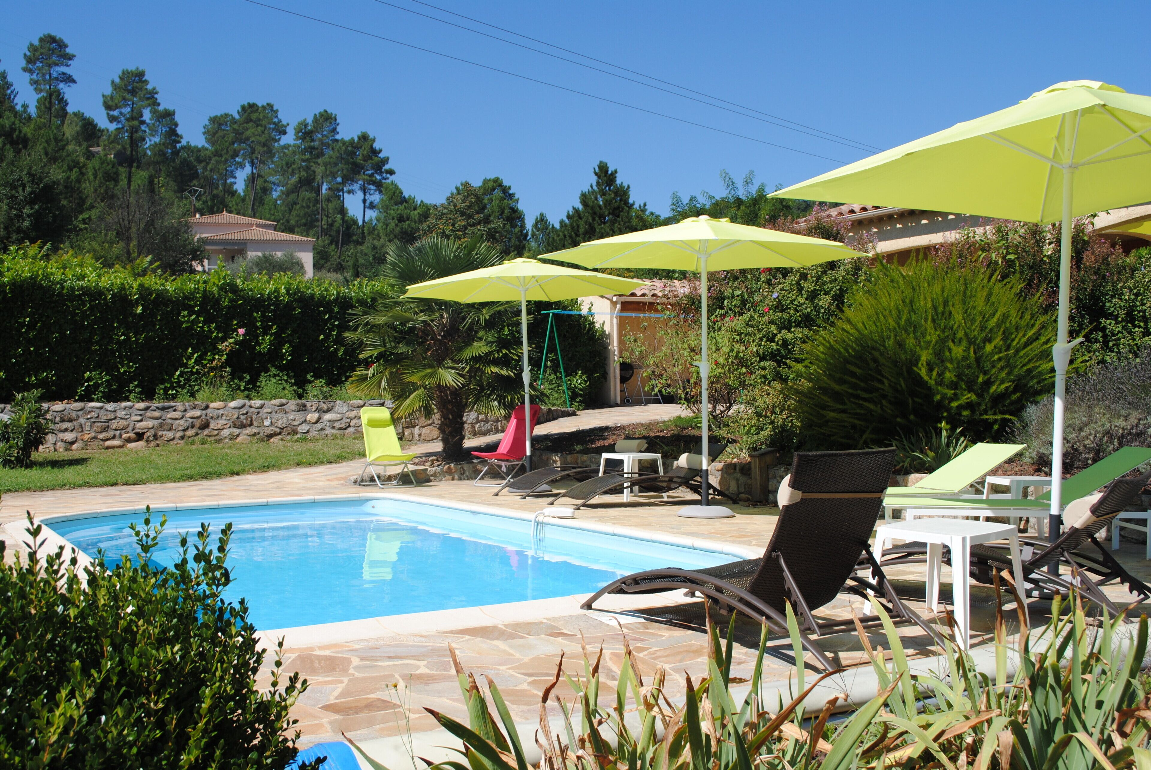 Une piscine entourée de verdure et d’un mur de pierre, avec des chaises longues et des parasols à proximité.