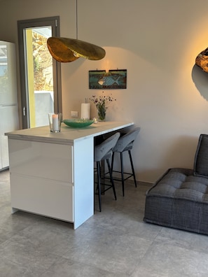 A modern kitchen with a central island, bar stools, a hanging light fixture, and a decorative wall sign.