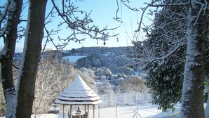 A snow-covered gazebo with a table and chairs, surrounded by trees and a snowy landscape.