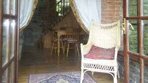 An open doorway leading to a room with a brick wall, a wooden staircase, a wicker chair, and a patterned rug.