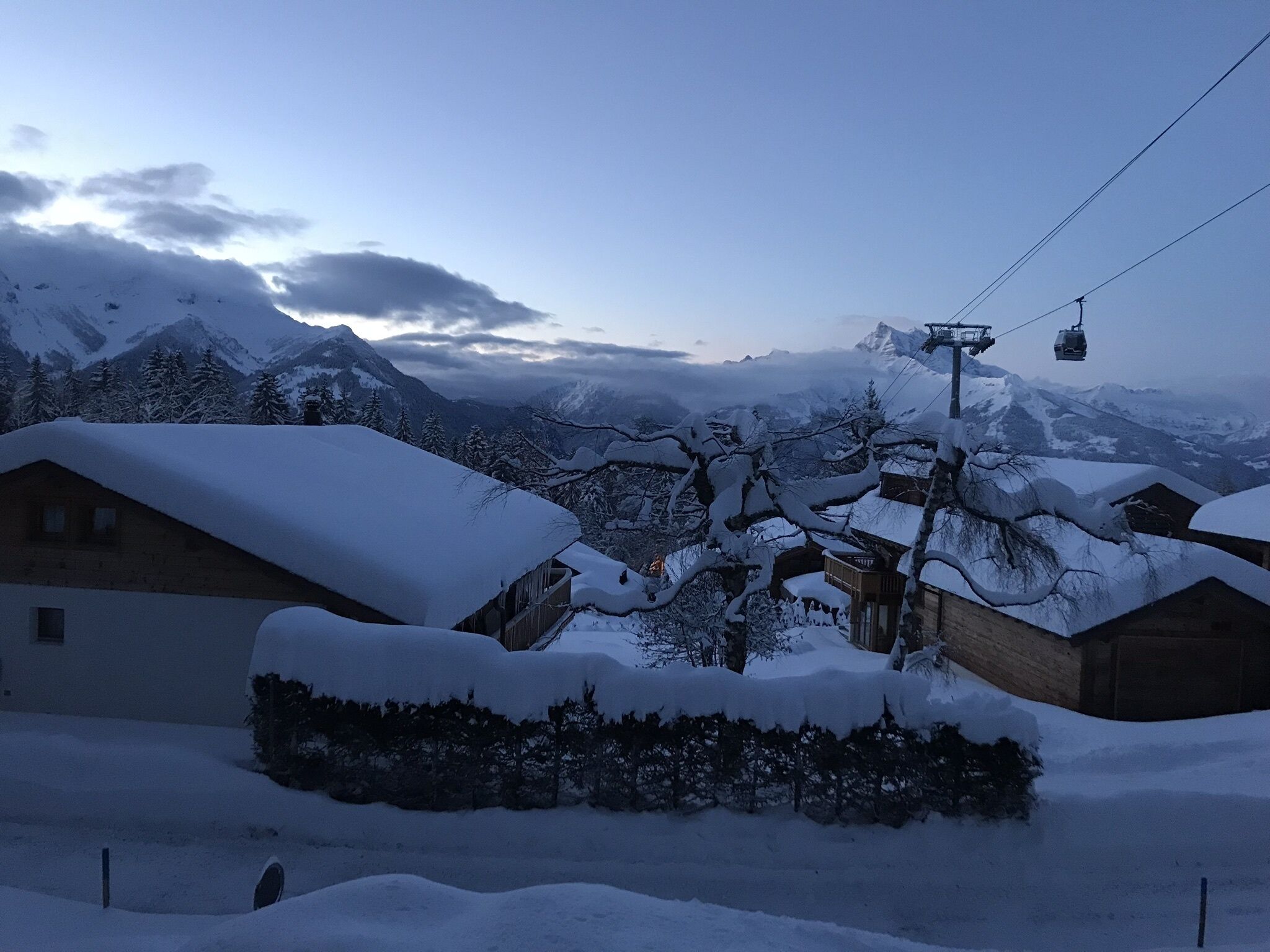 Un village de montagne enneigé, avec des bâtiments en bois et un télésiège.