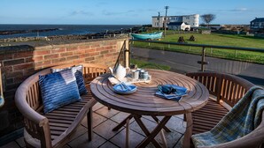 A wooden table and chairs on a balcony with a view of the sea and a boat. - Benthall House - sleeps 8 guests  in 4 bedrooms (Beadnell)