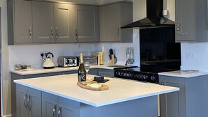 A modern kitchen with grey cabinets, a central island, and built-in appliances. - Benthall House - sleeps 8 guests  in 4 bedrooms (Beadnell)