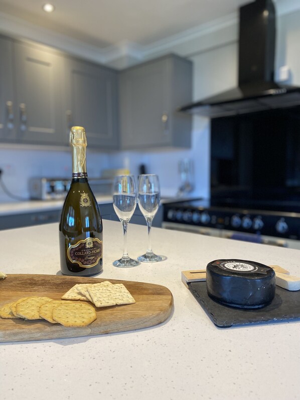 A kitchen counter with a bottle of champagne, two glasses, crackers, and a cheese wheel.