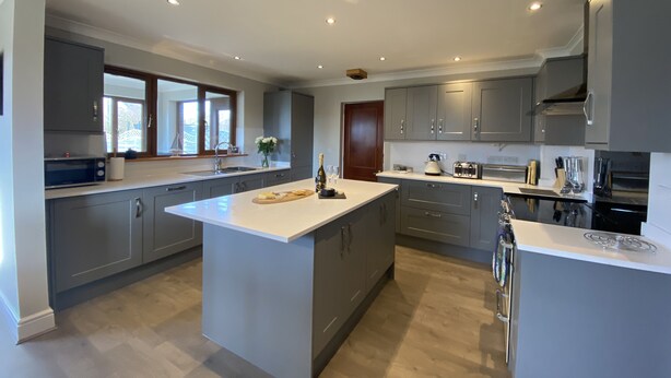 A modern kitchen with grey cabinets, a large island, and built-in appliances. - Benthall House - sleeps 8 guests  in 4 bedrooms (Beadnell)