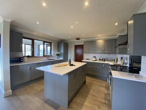A modern kitchen with grey cabinets, a large island, and built-in appliances. - Benthall House - sleeps 8 guests  in 4 bedrooms (Beadnell)
