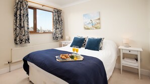 A neatly made bed with a dark blue bedspread, a tray of croissants, and orange juice on the nightstand. - Benthall House - sleeps 8 guests  in 4 bedrooms (Beadnell)