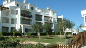 A multi-story hotel with balconies, a well-maintained lawn, and a wooden fence. - 2 Bedroom Penthouse Apartment With Large Sun Terrace (Torre-Pacheco)