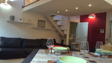 Zona pranzo con tavolo in legno apparecchiato per quattro persone, una scala e una parete di accento rossa.
