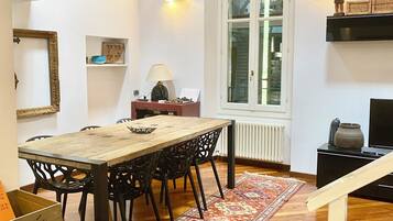 A dining area with a wooden table, black chairs, a patterned rug, and a window with blinds.