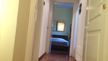 Ein Flur mit Holzboden, der zu einem Schlafzimmer mit Bett und Nachttisch führt.
