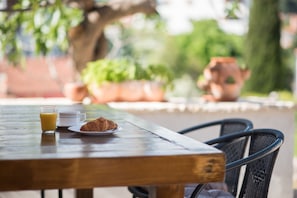 A wooden table with a glass of orange juice, a cup, and a croissant.