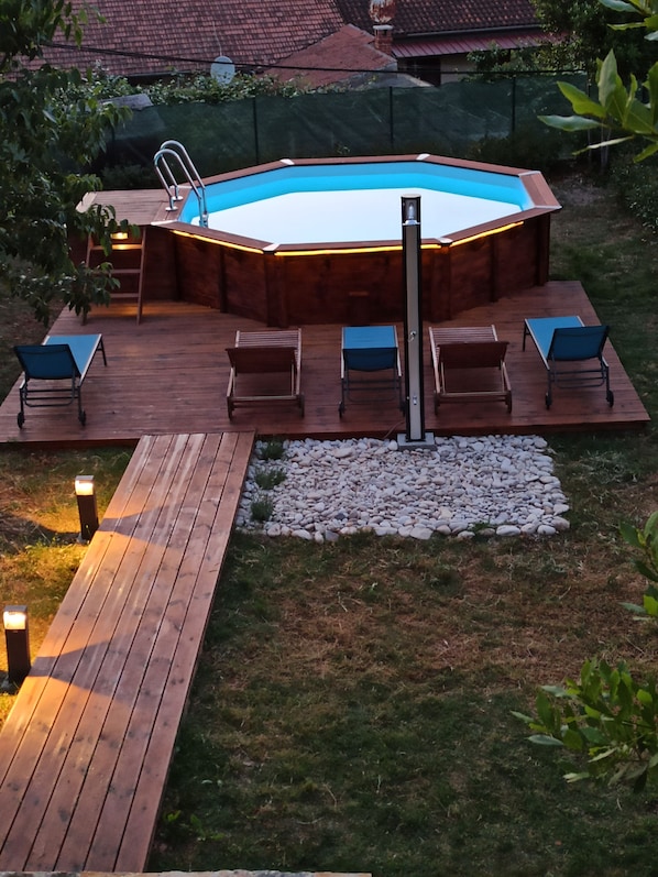 An outdoor swimming pool with a wooden deck, lounge chairs, and a hot tub.