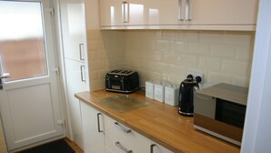 Una cocina con armarios blancos, encimera de madera, un tostador, un hervidor y una cafetera.