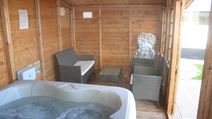 Una cabaña de madera con jacuzzi, mobiliario de mimbre y una mesita.