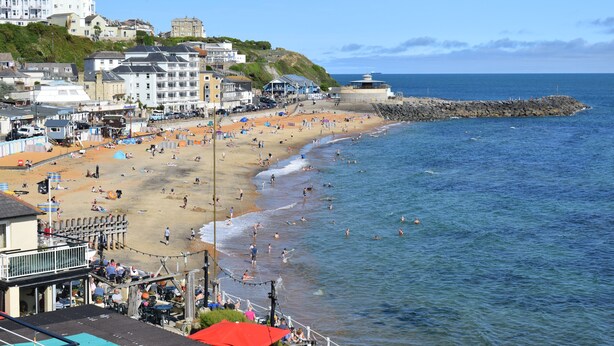 Eine K üstenstadt mit Sandstrand, einem Felssteg und Häusern entlang der Küste.