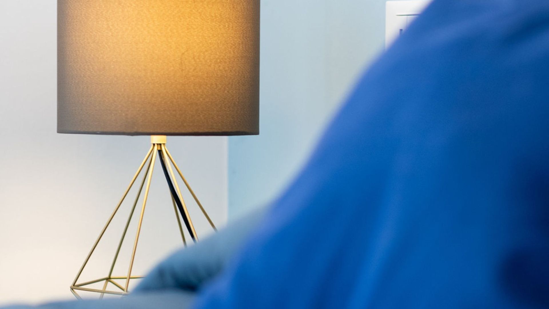 A modern lamp with a gold base and a large, textured shade on a bedside table.