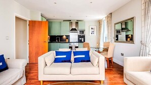 Uma sala de estar moderna com sofá, mesa de jantar e cozinha ao fundo.