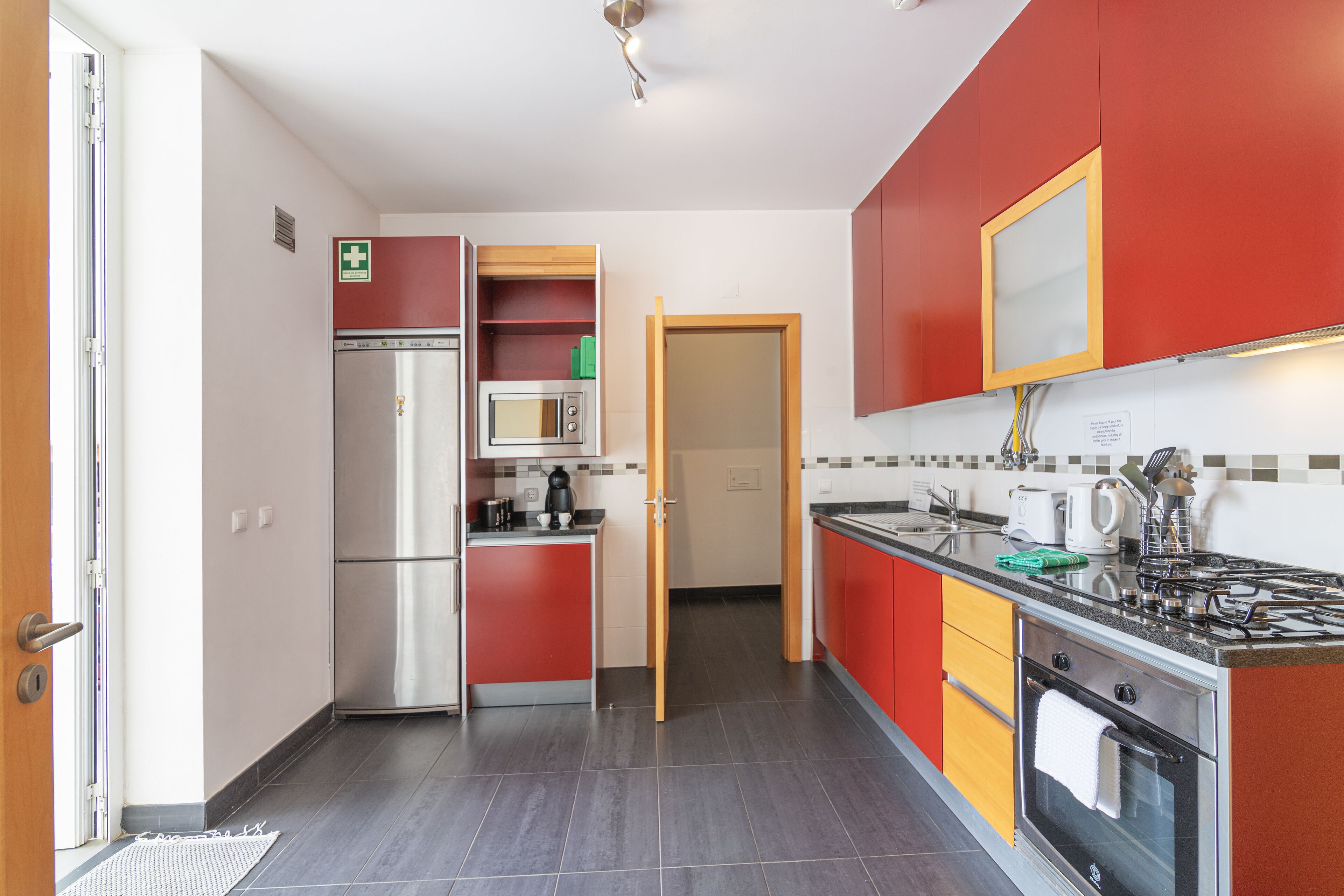 Een moderne keuken met rode en gele kasten, roestvrijstalen apparatuur en een betegelde achterwand.