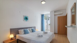 A neatly made bed with white linens and blue pillows, a bedside lamp, and a wall-mounted air conditioner. - Luxury Spacious 3 Bedroom Duplex Apartment With Sea Views & Salt Water Pool! (Loulé)