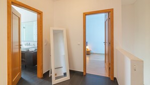 A hallway with a mirror, a door leading to a bathroom, and a view of a bedroom. - Luxury Spacious 3 Bedroom Duplex Apartment With Sea Views & Salt Water Pool! (Loulé)