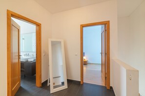 A hallway with a mirror, a door leading to a bathroom, and a view of a bedroom.