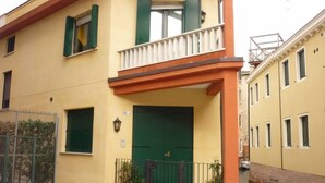 Un edificio amarillo con puerta verde, un balcón y un pequeño jardín con macetas.