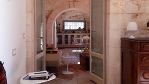 An open-plan living area with a stone archway, a dining table, and a kitchen in the background. - Stylish luxury trulli with private pool and amazing sea view  (Ostuni)