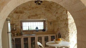 A rustic kitchen with stone walls, a window, a sink, and a dining area with chairs and a table. - Stylish luxury trulli with private pool and amazing sea view  (Ostuni)