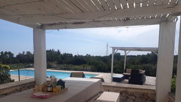 Um pátio externo com piscina, piso de pedra e uma mesa posta.