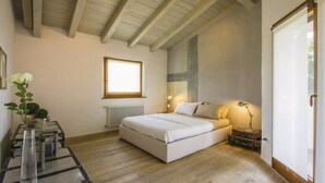 A bedroom with a large bed, a window, a radiator, and a bedside table with a lamp. - Capriva Del Friuli: House / Villa - Capriva del Friuli (Capriva del Friuli)