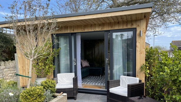Een moderne buitenpatio met rieten meubels en een glazen deur naar de binnenruimte.