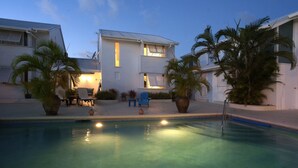 A pool area with a clear pool, lounge chairs, and a building with multiple windows. - Charming townhouse only 10 minutes from the beach! (Porters)