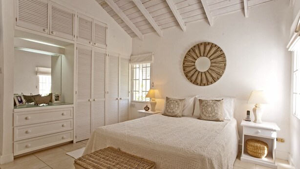 A bedroom with a large bed, a wardrobe, a mirror, a round wall decoration, and a bedside table with a lamp. - Charming townhouse only 10 minutes from the beach! (Porters)
