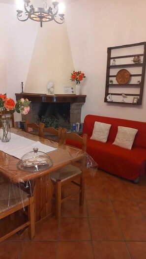 A dining area with a wooden table, chairs, a chandelier, a red sofa, and a fireplace. - Independent villa with exclusive property garden (Solanas)