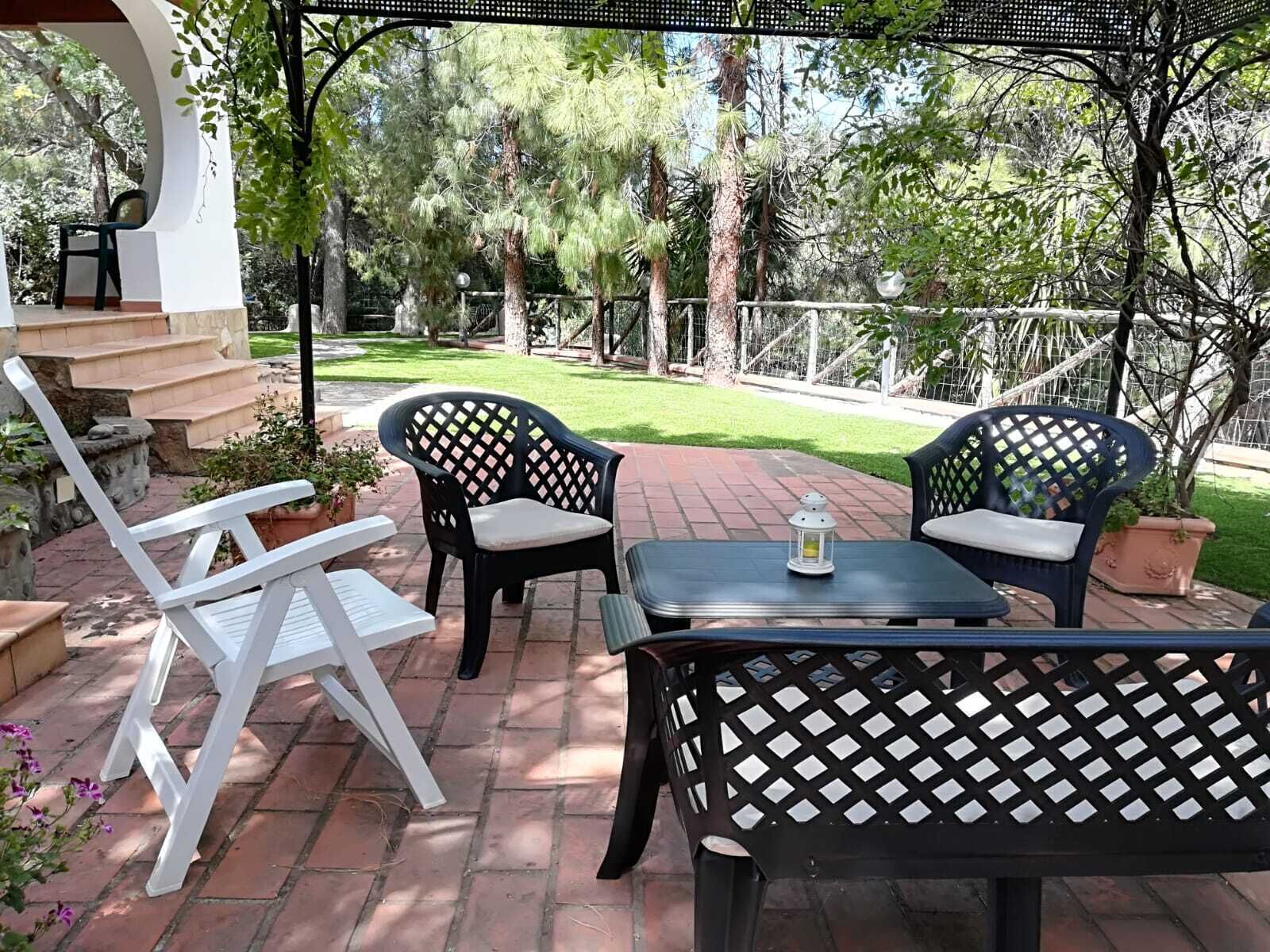 An outdoor patio area with a table and two chairs, surrounded by a brick pathway and greenery.