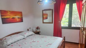 Un dormitorio con cama, mesita de noche, lámpara, cuadro, ventana con cortinas y puerta.