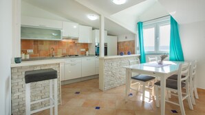Une cuisine moderne avec des meubles blancs, un pare-feu en pierre et un coin repas comprenant une table et des chaises blanches.